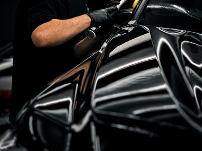 Gloved hands polishing glossy black paint with a machine polisher