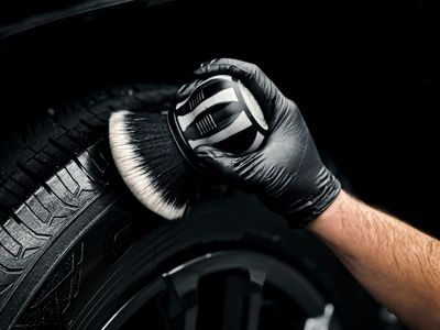 Gloved hand scrubbing a tire sidewall with a soft detailing brush