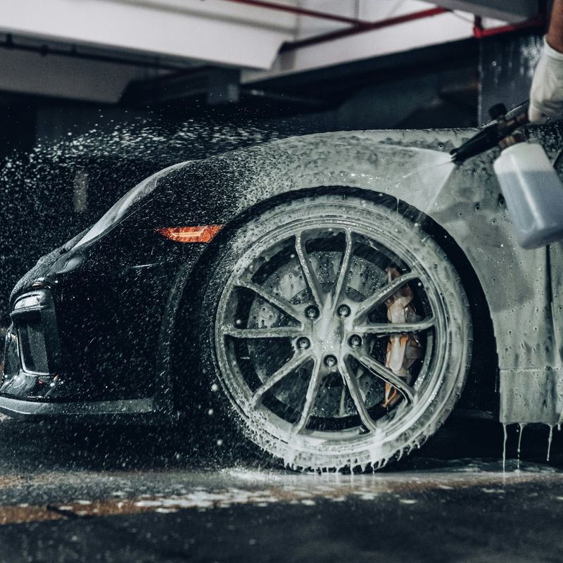 Black sports car with foam covering the front wheel during a hand wash in a garage