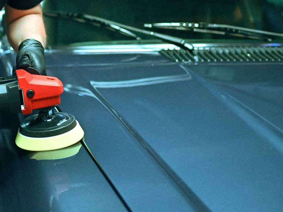 Machine polisher with a foam pad on the hood of a dark blue car