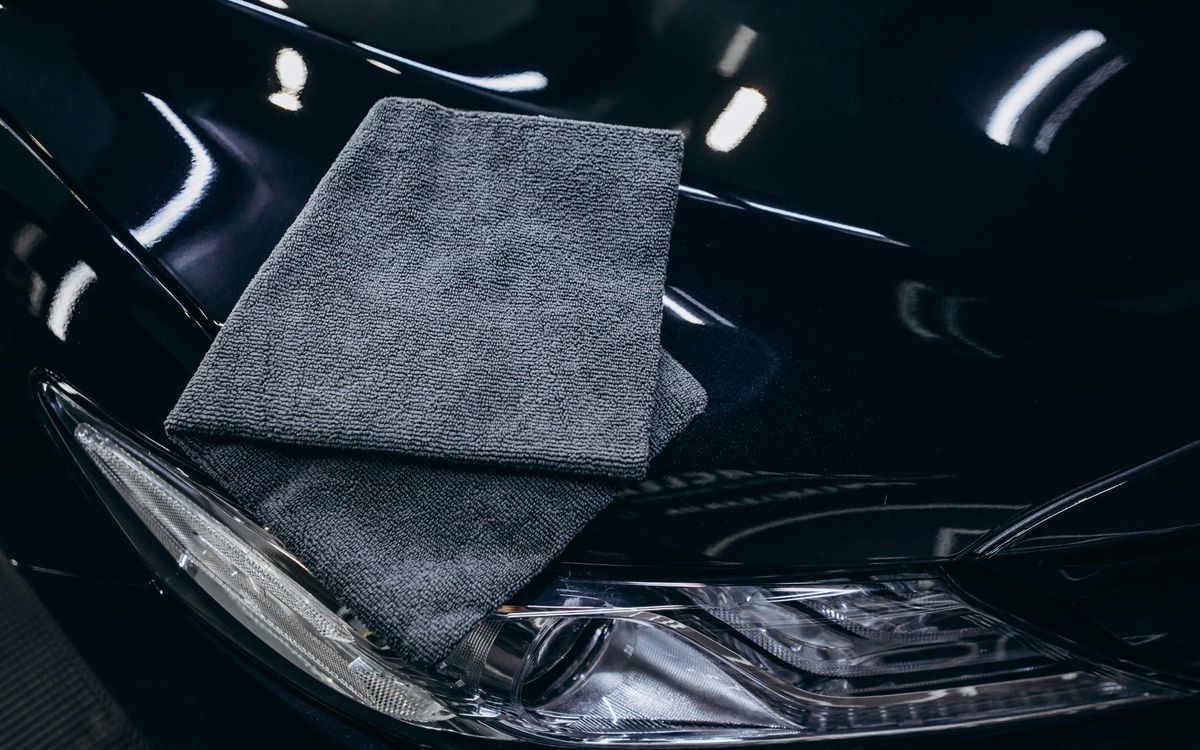 Gray microfiber towel resting on the glossy hood of a dark car, beside the headlight